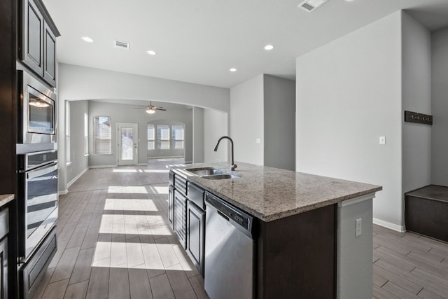 kitchen with ceiling fan, sink, light stone countertops, a kitchen island with sink, and appliances with stainless steel finishes