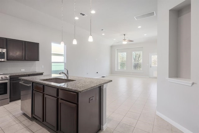 kitchen featuring ceiling fan, sink, decorative backsplash, a center island with sink, and appliances with stainless steel finishes