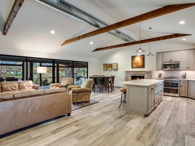 kitchen featuring gray cabinetry, appliances with stainless steel finishes, decorative light fixtures, a kitchen island, and a breakfast bar area