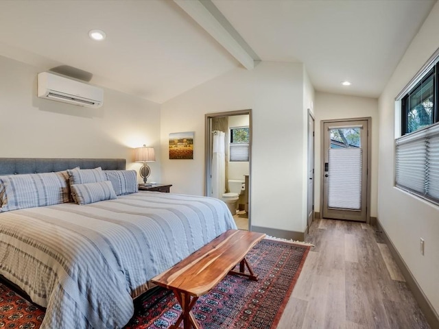 bedroom with hardwood / wood-style flooring, lofted ceiling with beams, a wall mounted AC, and ensuite bath