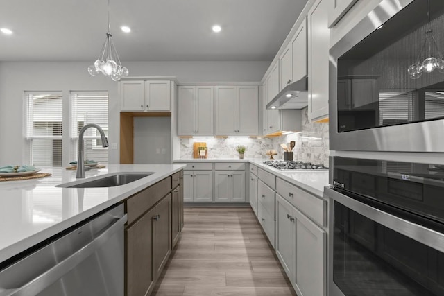 6304 Rotunda Vw, Austin, TX 78747 - kitchen with appliances with stainless steel finishes, light countertops, under cabinet range hood, a chandelier, and light wood finished floors