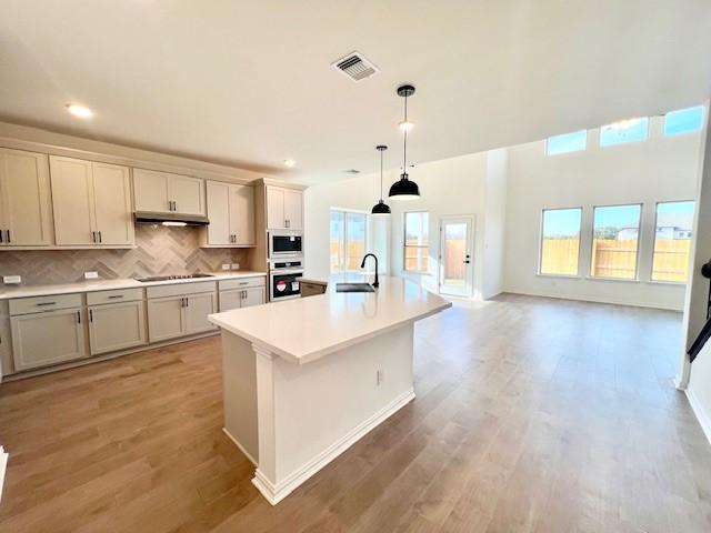 kitchen with stainless steel oven, black electric cooktop, built in microwave, sink, and an island with sink