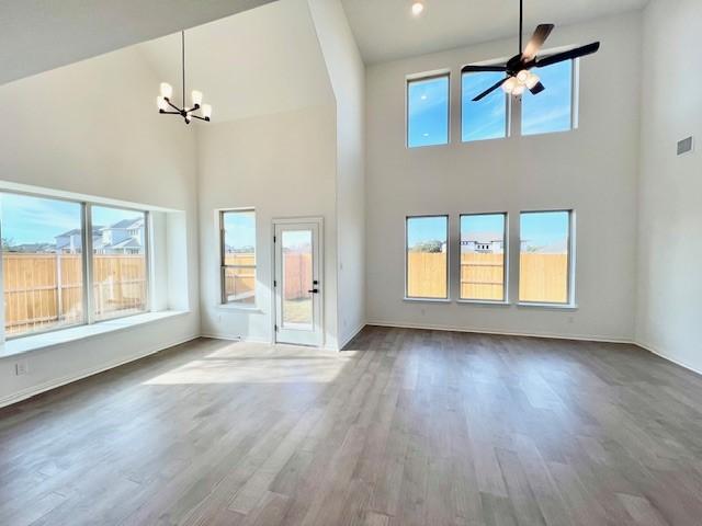 unfurnished living room with ceiling fan with notable chandelier, wood-type flooring, and a high ceiling