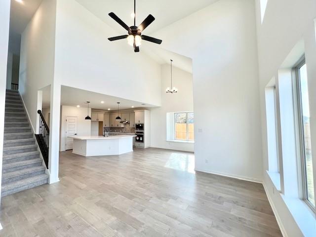 unfurnished living room with ceiling fan with notable chandelier, a healthy amount of sunlight, wood-type flooring, and high vaulted ceiling