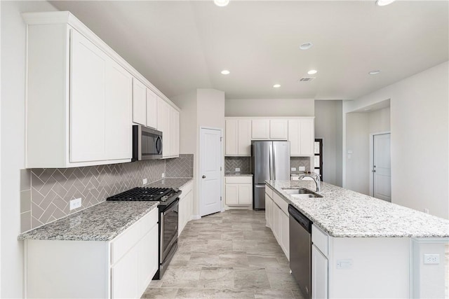 kitchen with light stone countertops, sink, a kitchen island with sink, white cabinets, and appliances with stainless steel finishes