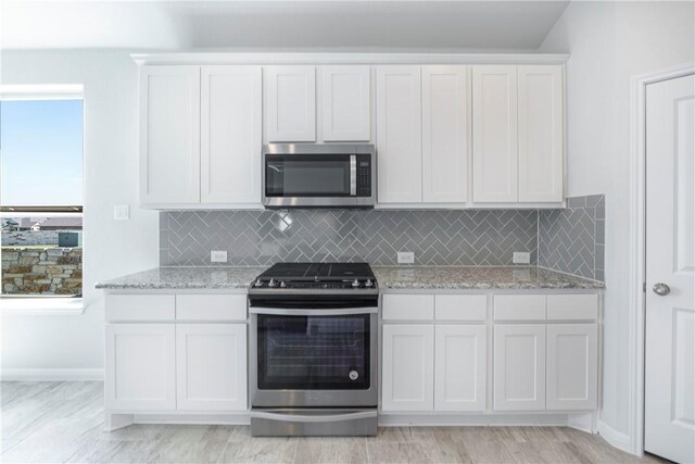 kitchen featuring light stone countertops, appliances with stainless steel finishes, backsplash, light hardwood / wood-style floors, and white cabinetry