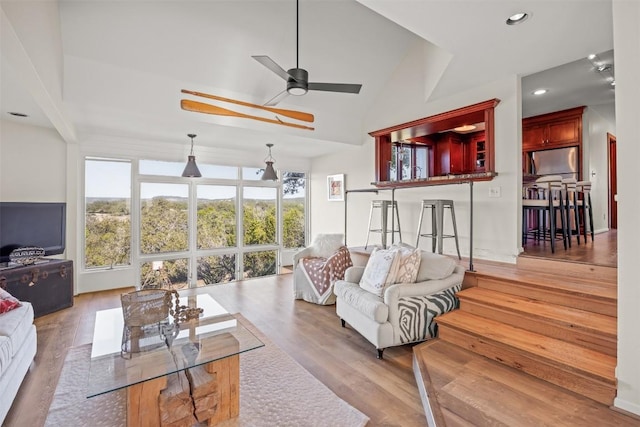 living room with ceiling fan, vaulted ceiling, and light wood-type flooring