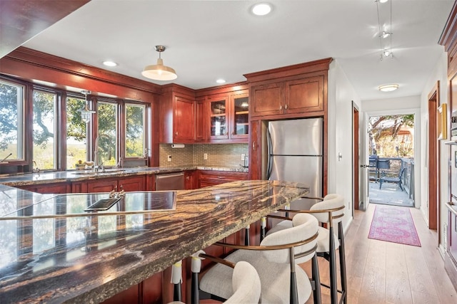 kitchen featuring sink, backsplash, decorative light fixtures, appliances with stainless steel finishes, and light wood-type flooring