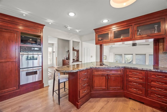 kitchen with a kitchen bar, light stone counters, kitchen peninsula, and light wood-type flooring