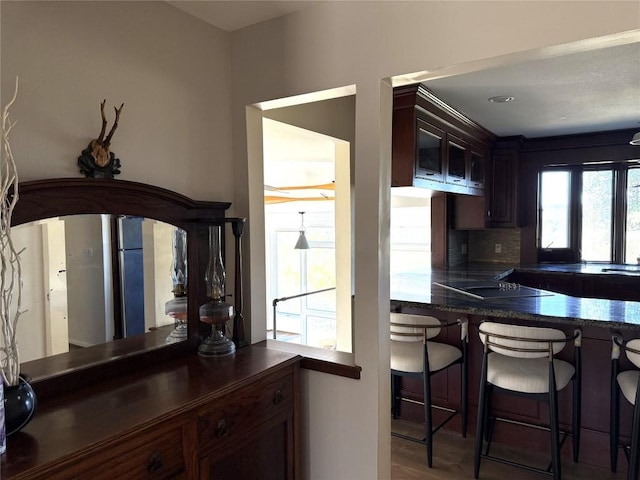 kitchen featuring a kitchen breakfast bar, backsplash, black electric stovetop, dark brown cabinets, and hardwood / wood-style floors