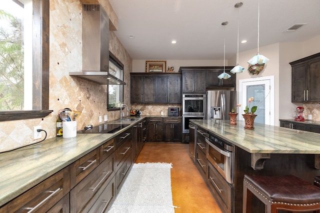 kitchen with a breakfast bar, dark brown cabinets, stainless steel appliances, and wall chimney range hood