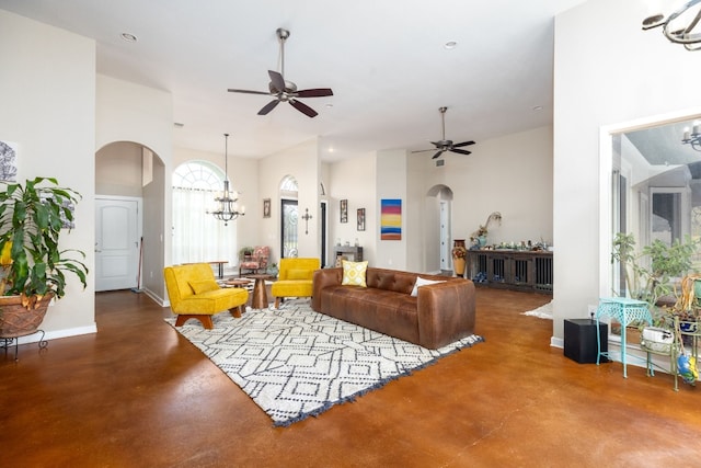 living room with concrete flooring, a high ceiling, and ceiling fan with notable chandelier