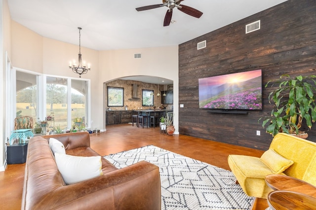 living room with a high ceiling, ceiling fan with notable chandelier, and wooden walls