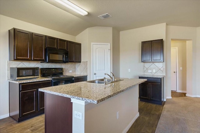 kitchen with tasteful backsplash, sink, black appliances, and a center island with sink