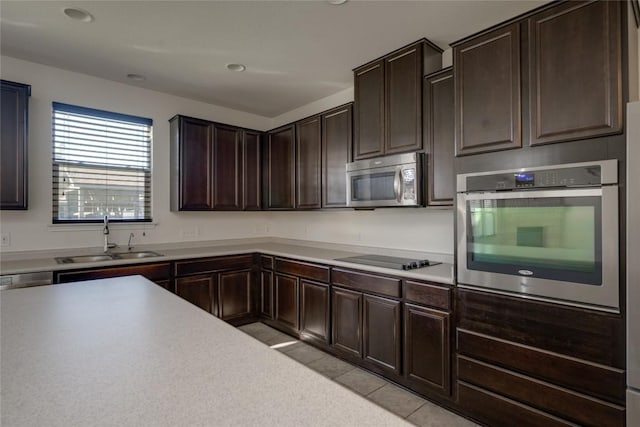 kitchen featuring sink, light tile patterned floors, stainless steel appliances, and dark brown cabinetry