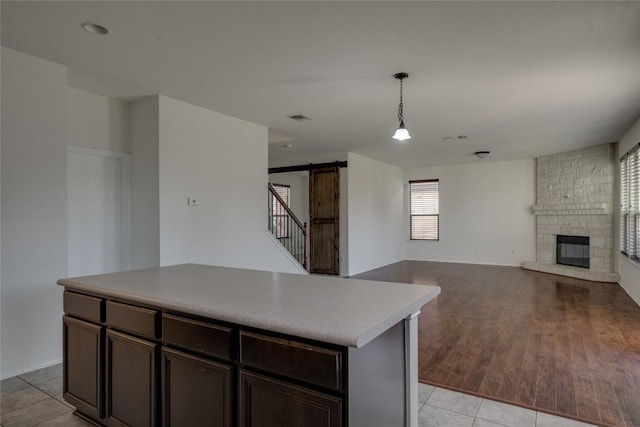 kitchen with a stone fireplace, hanging light fixtures, a barn door, light tile patterned floors, and a kitchen island