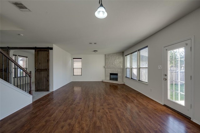 unfurnished living room featuring wood-type flooring, a barn door, and a stone fireplace