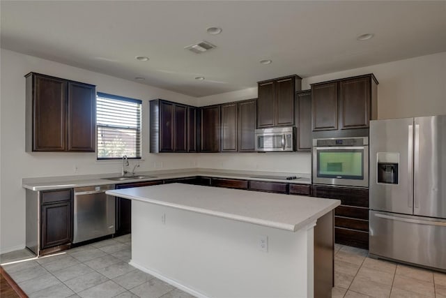 kitchen with appliances with stainless steel finishes, dark brown cabinets, sink, light tile patterned floors, and a kitchen island