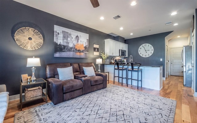 living room featuring light wood-type flooring, ceiling fan, and sink