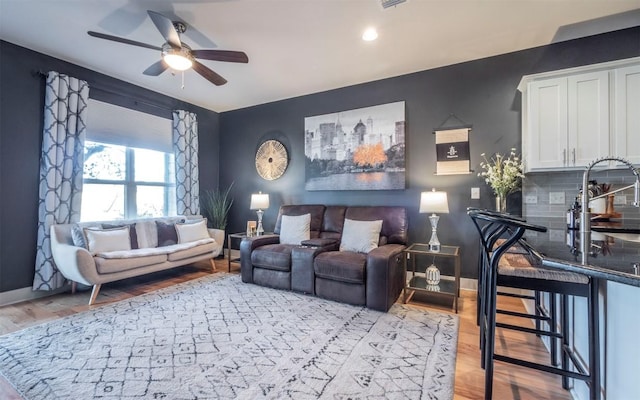 living room with ceiling fan, sink, and light wood-type flooring