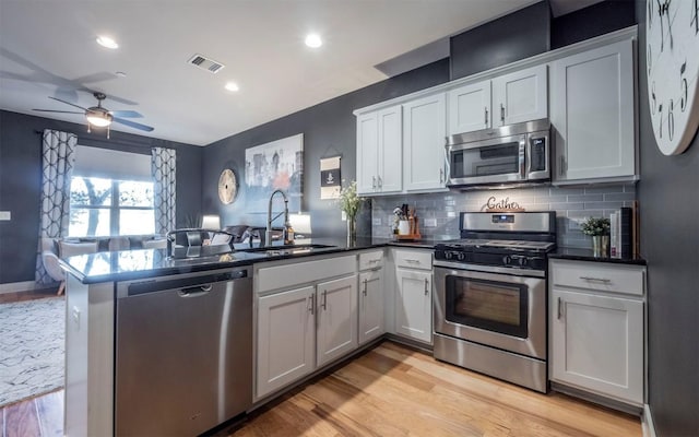 kitchen with kitchen peninsula, stainless steel appliances, sink, light hardwood / wood-style flooring, and white cabinets