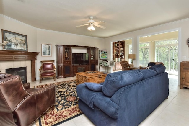 living room featuring a tiled fireplace, ceiling fan, crown molding, and light tile patterned floors