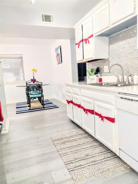 kitchen with decorative backsplash, sink, light hardwood / wood-style flooring, dishwasher, and white cabinetry