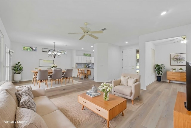 living room with ceiling fan with notable chandelier and light hardwood / wood-style floors