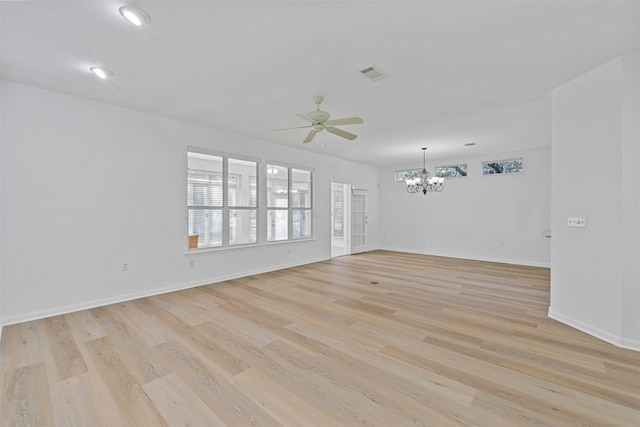 spare room with a wealth of natural light, ceiling fan with notable chandelier, and light wood-type flooring