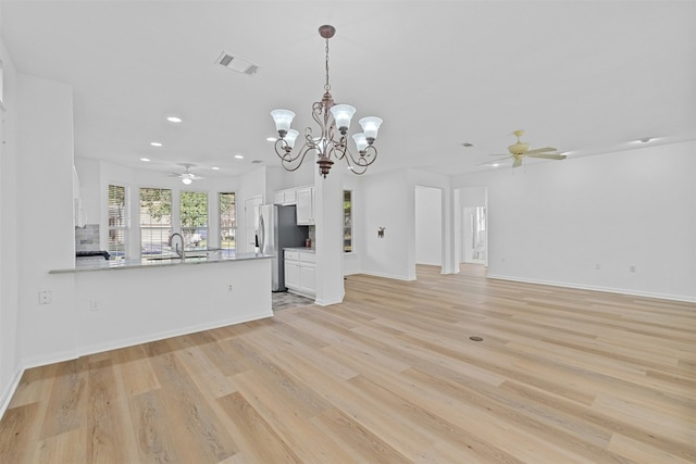 unfurnished living room with ceiling fan with notable chandelier, sink, and light hardwood / wood-style flooring