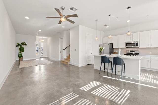 kitchen with a kitchen island with sink, ceiling fan, decorative light fixtures, white cabinetry, and stainless steel appliances