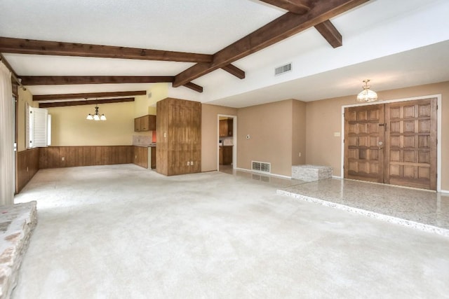 carpeted empty room with beam ceiling, an inviting chandelier, and wooden walls