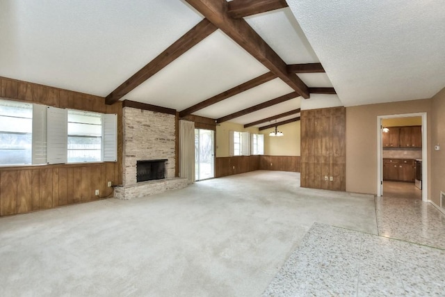 unfurnished living room featuring lofted ceiling with beams, light colored carpet, a textured ceiling, wooden walls, and a fireplace