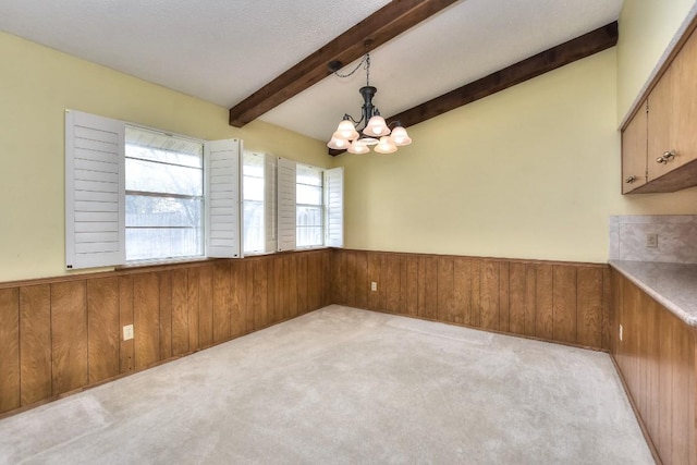 unfurnished dining area with beam ceiling, an inviting chandelier, and wood walls