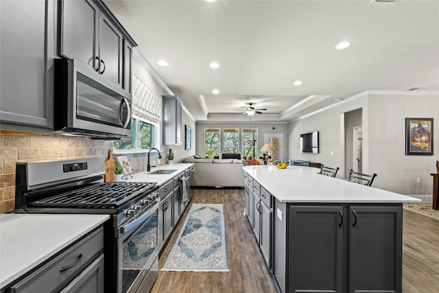 kitchen featuring a kitchen island, appliances with stainless steel finishes, open floor plan, light countertops, and crown molding