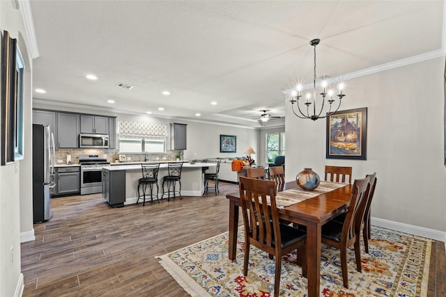 dining space featuring dark wood-style flooring, visible vents, ornamental molding, baseboards, and ceiling fan with notable chandelier