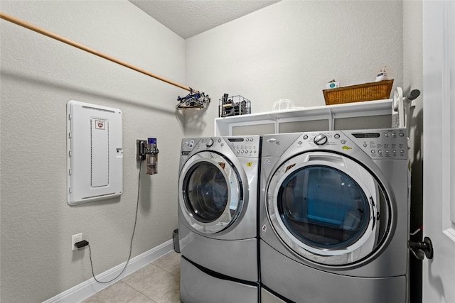 clothes washing area featuring light tile patterned floors, laundry area, baseboards, electric panel, and washing machine and clothes dryer