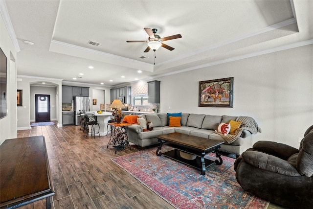 living room with dark wood-type flooring, a tray ceiling, visible vents, and a ceiling fan