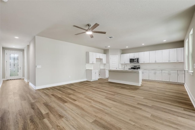 kitchen with appliances with stainless steel finishes, a kitchen island with sink, sink, white cabinets, and light hardwood / wood-style floors