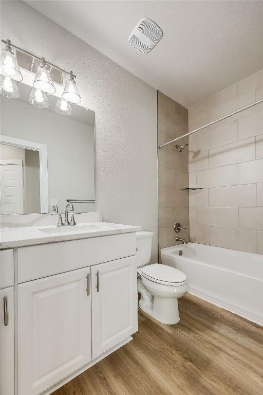 full bathroom featuring vanity, hardwood / wood-style floors, tiled shower / bath combo, and toilet