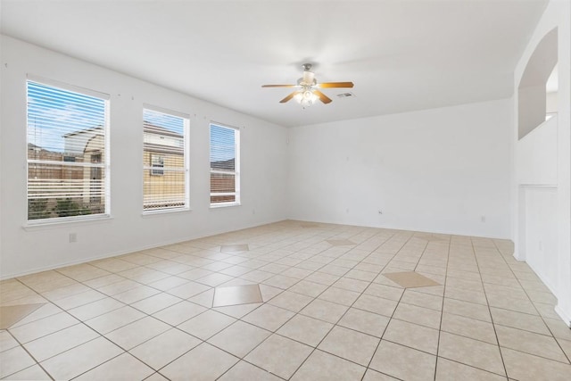 empty room with arched walkways, a ceiling fan, and light tile patterned flooring
