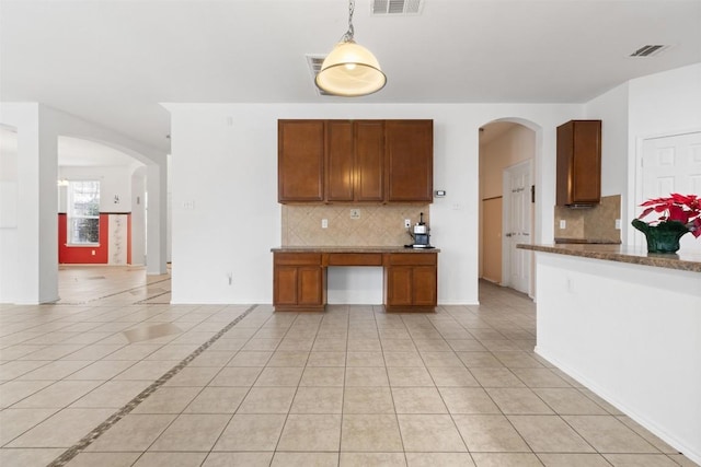 kitchen featuring brown cabinetry, arched walkways, decorative light fixtures, and light tile patterned floors