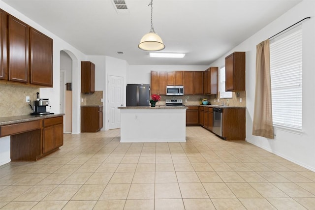 kitchen featuring pendant lighting, stainless steel appliances, visible vents, decorative backsplash, and brown cabinetry