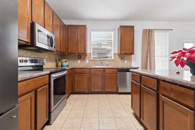 kitchen featuring light tile patterned floors, decorative backsplash, appliances with stainless steel finishes, brown cabinetry, and a sink