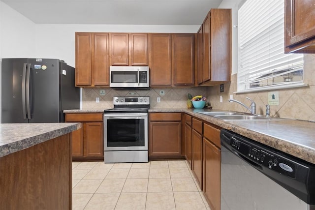 kitchen featuring stainless steel appliances, decorative backsplash, brown cabinetry, light tile patterned flooring, and a sink