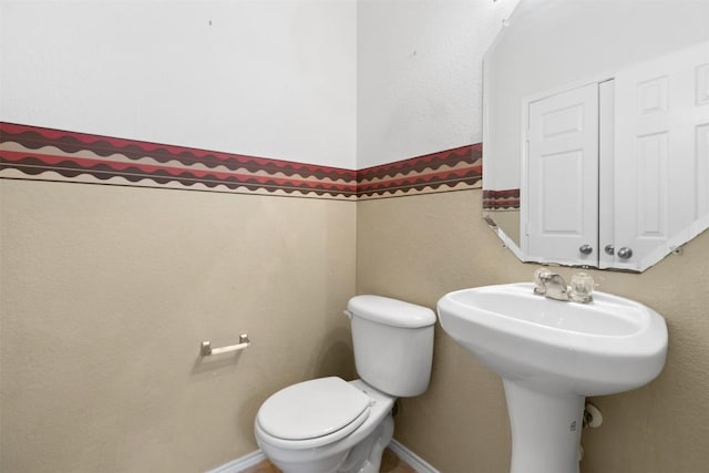 half bath featuring toilet, baseboards, and a sink