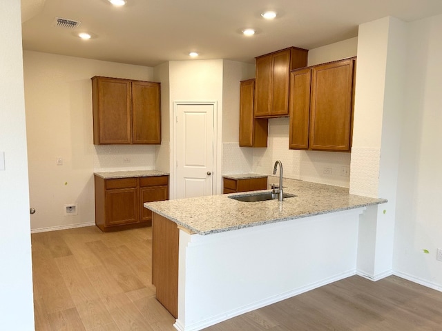 kitchen featuring light hardwood / wood-style floors, sink, light stone countertops, and kitchen peninsula