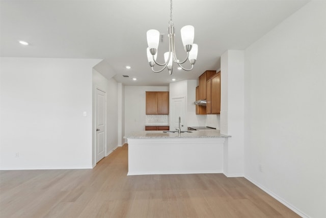 14013 Vigilance St, Manor, TX 78653 - kitchen with brown cabinets, tasteful backsplash, light wood-type flooring, a chandelier, and under cabinet range hood
