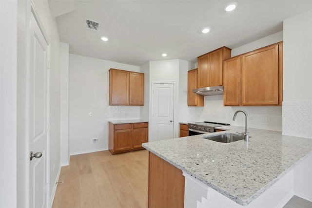 14013 Vigilance St, Manor, TX 78653 - kitchen featuring under cabinet range hood, stainless steel range with electric stovetop, brown cabinetry, a peninsula, and recessed lighting