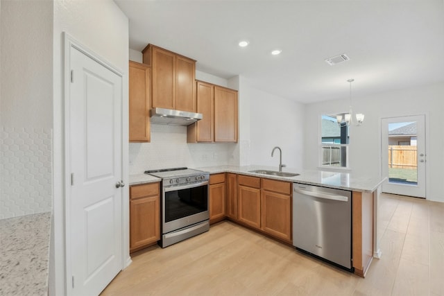 14013 Vigilance St, Manor, TX 78653 - kitchen with stainless steel appliances, under cabinet range hood, a peninsula, light wood-style flooring, and backsplash